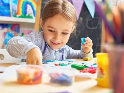 Portrait of smiling little girl working with plasticine in art and craft class of development school